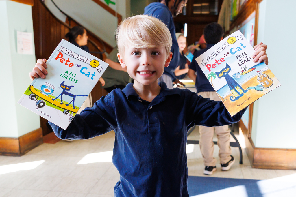 A young student holds up to books while flashing a big smile. 