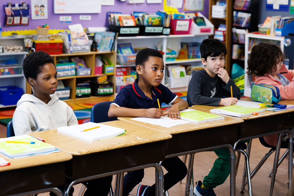 Children sit at desks in a colorful classroom, engaged in learning activities.