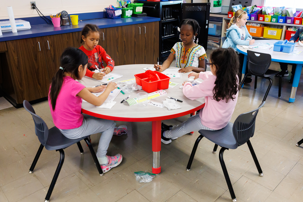 Four young students are seated around a round table, engaged in a learning activity.