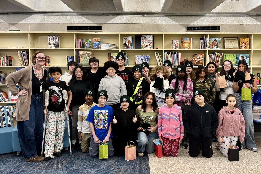 A diverse group of students and a teacher pose for a photo in a library, surrounded by bookshelves.