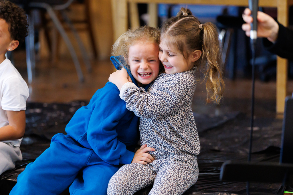 Two young students share a hug during a school assembly.