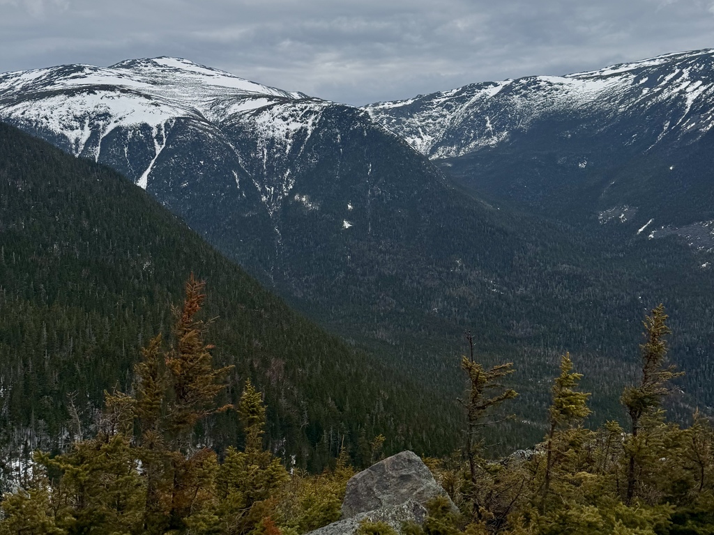A vast mountain range with snow-capped peaks under a cloudy sky.