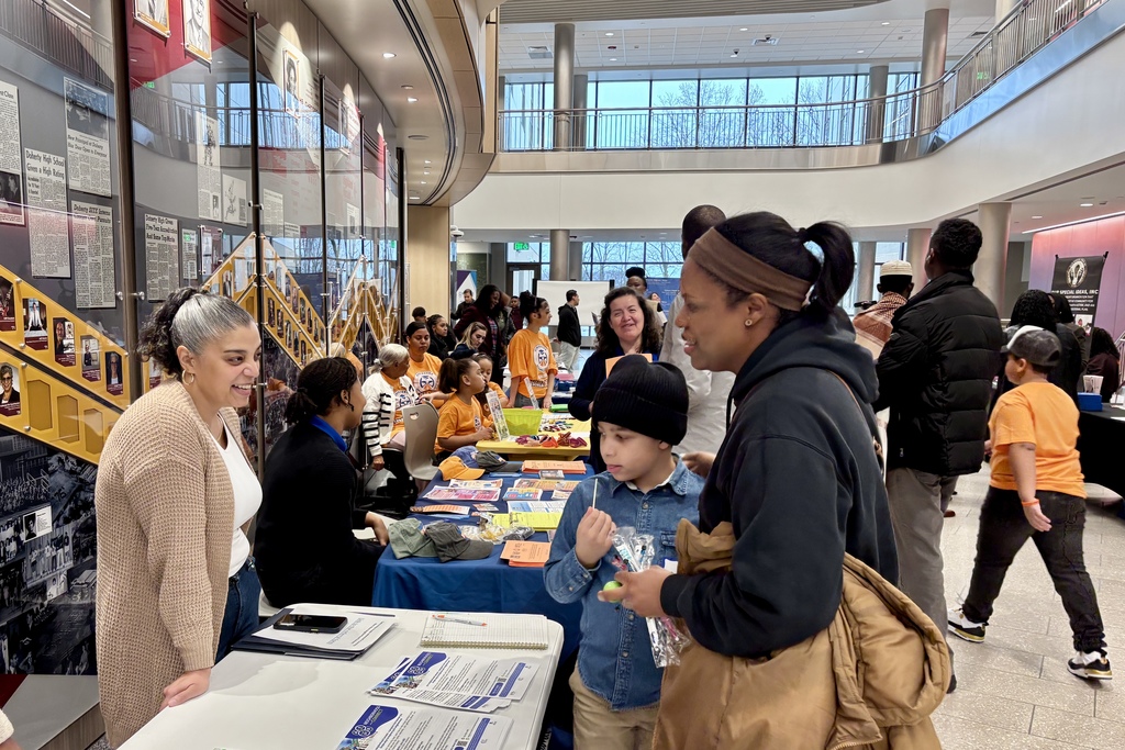 People gather at tables with informational brochures and displays in a bright, modern building.