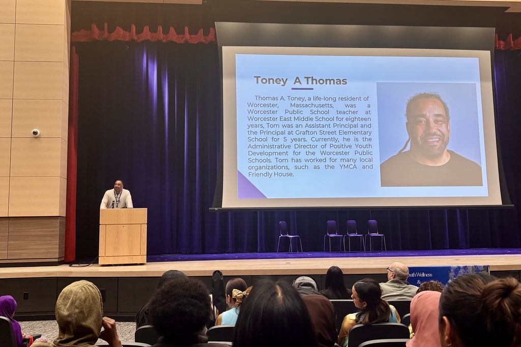 A man stands at a podium on a stage, presenting to an audience in an auditorium.