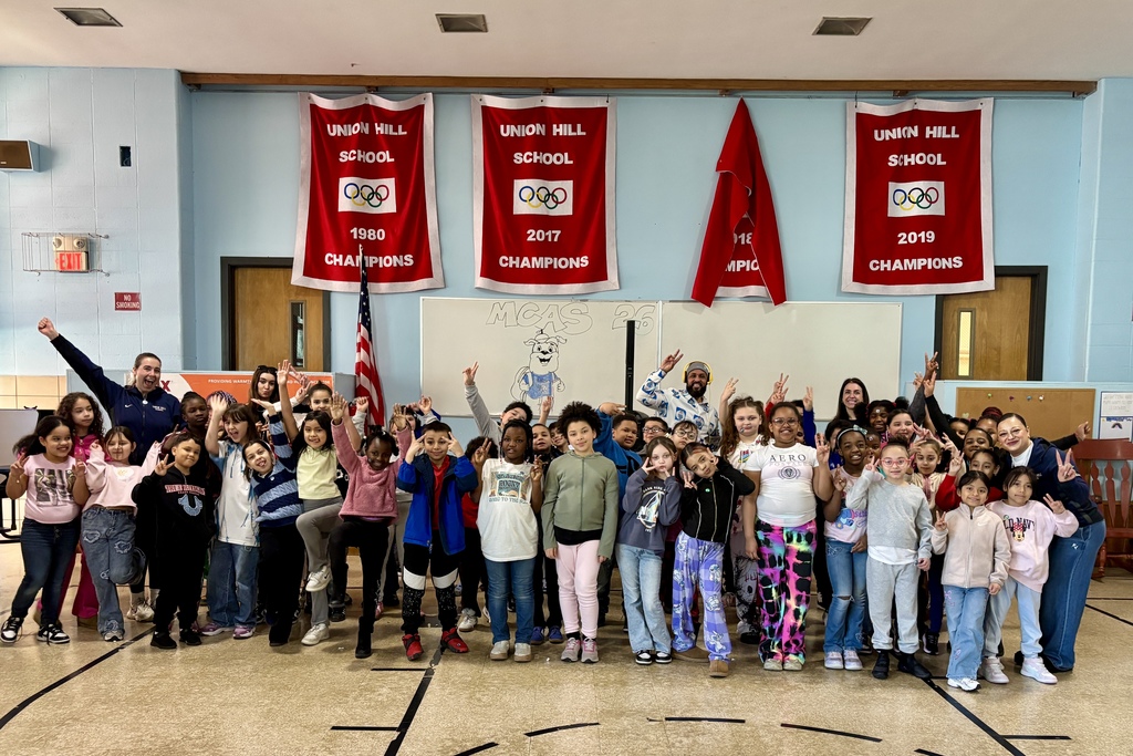A large group of smiling students and adults pose for a photo in front of banners celebrating Union Hill School's championship wins.