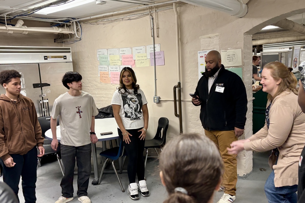 A group of young people and adults stand in a room with motivational posters on the wall.
