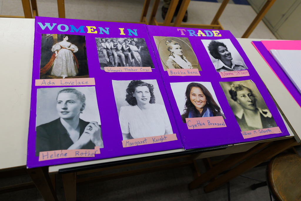 A purple display board titled 'WOMEN IN TRADE' features portraits of notable women like Ada Lovelace and Bertha Benz.
