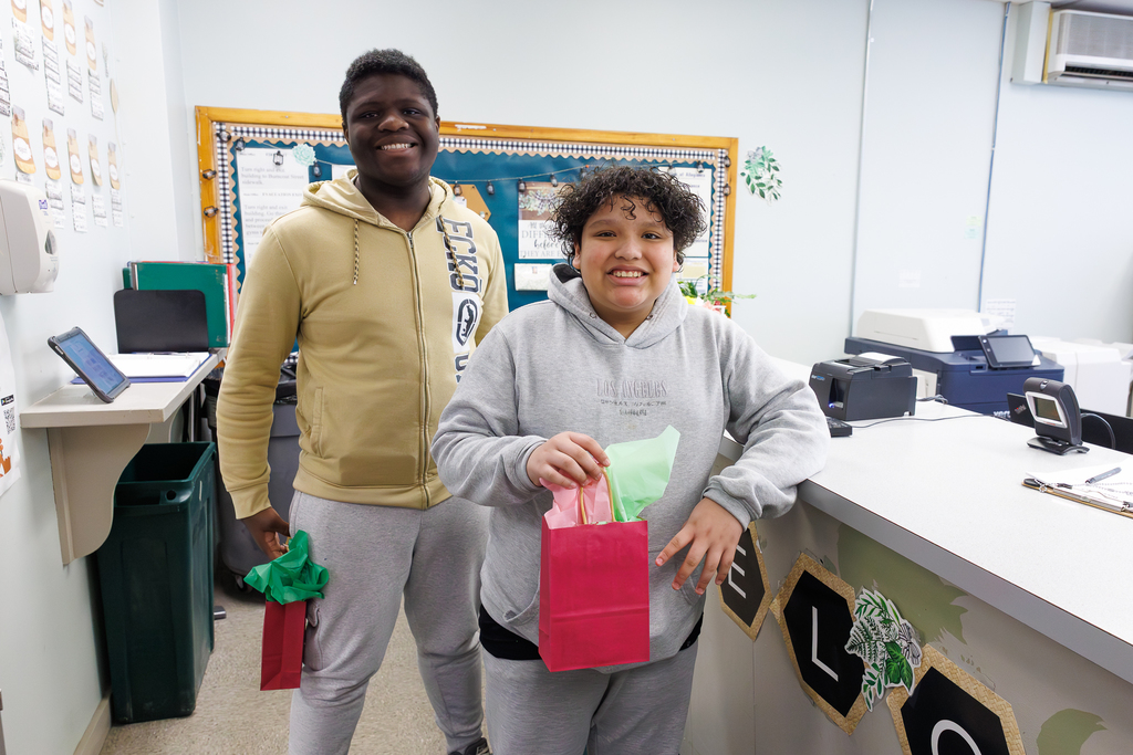 Two students stand together, each holding a gift bag filled with colorful tissue paper.