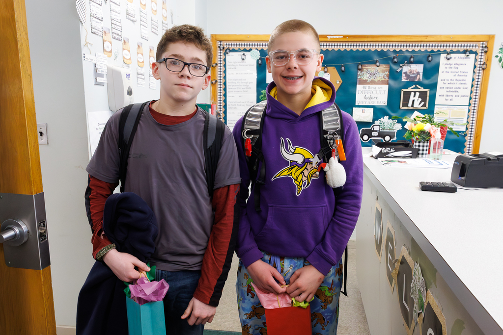 Two students stand together, each holding a gift bag filled with colorful tissue paper.