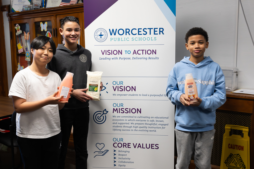 Four children stand together, holding toiletries for a school drive.