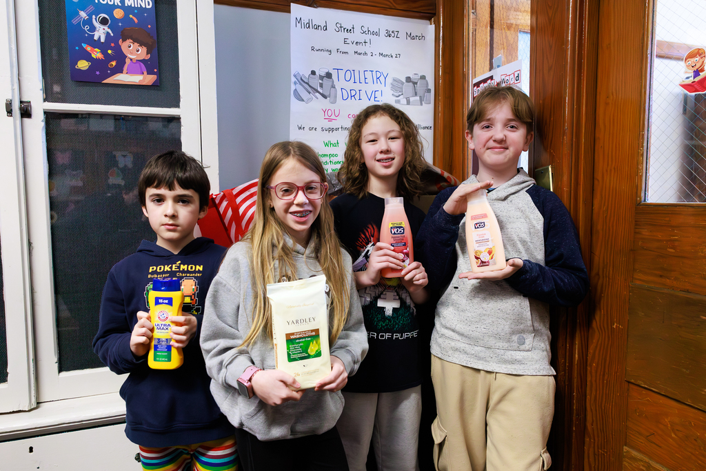 Four children stand together, holding toiletries for a school drive.