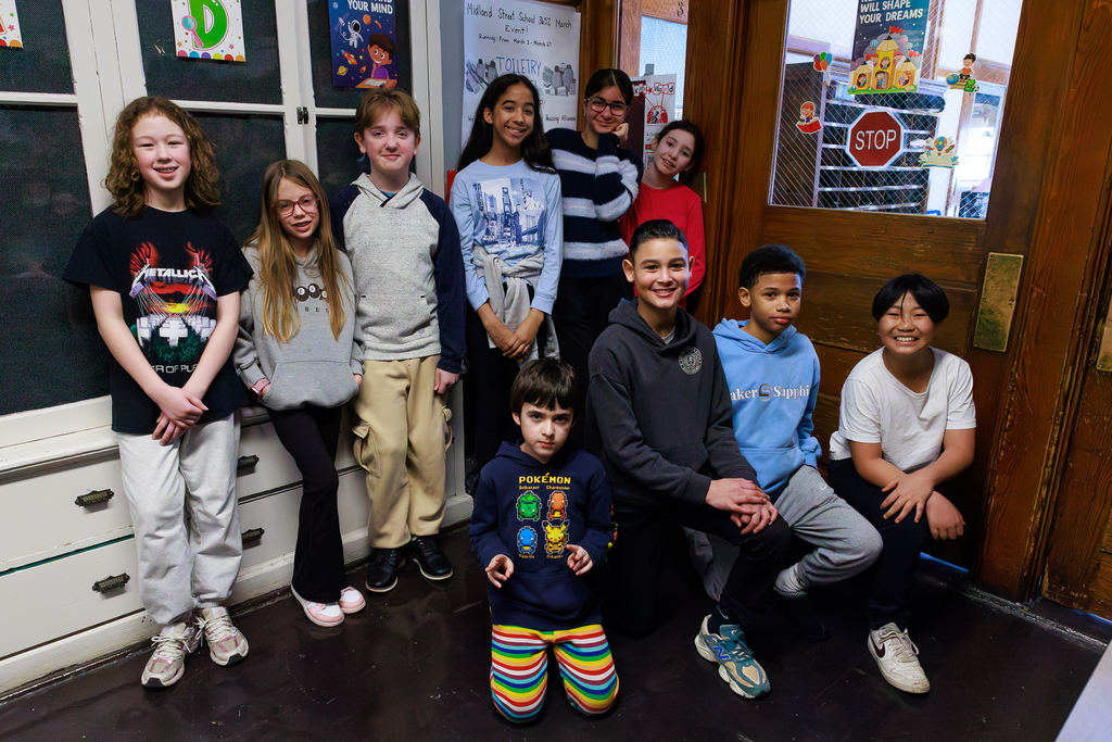 A group of students pose for a photo in a school hallway, with colorful posters on the walls.