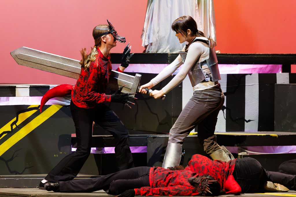 Two performers in costume engage in a staged sword fight on a theatrical stage.
