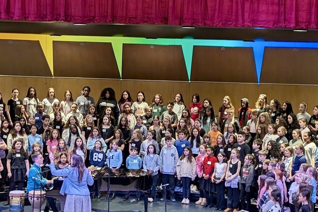 A large choir of children and young adults stands on risers, facing forward.