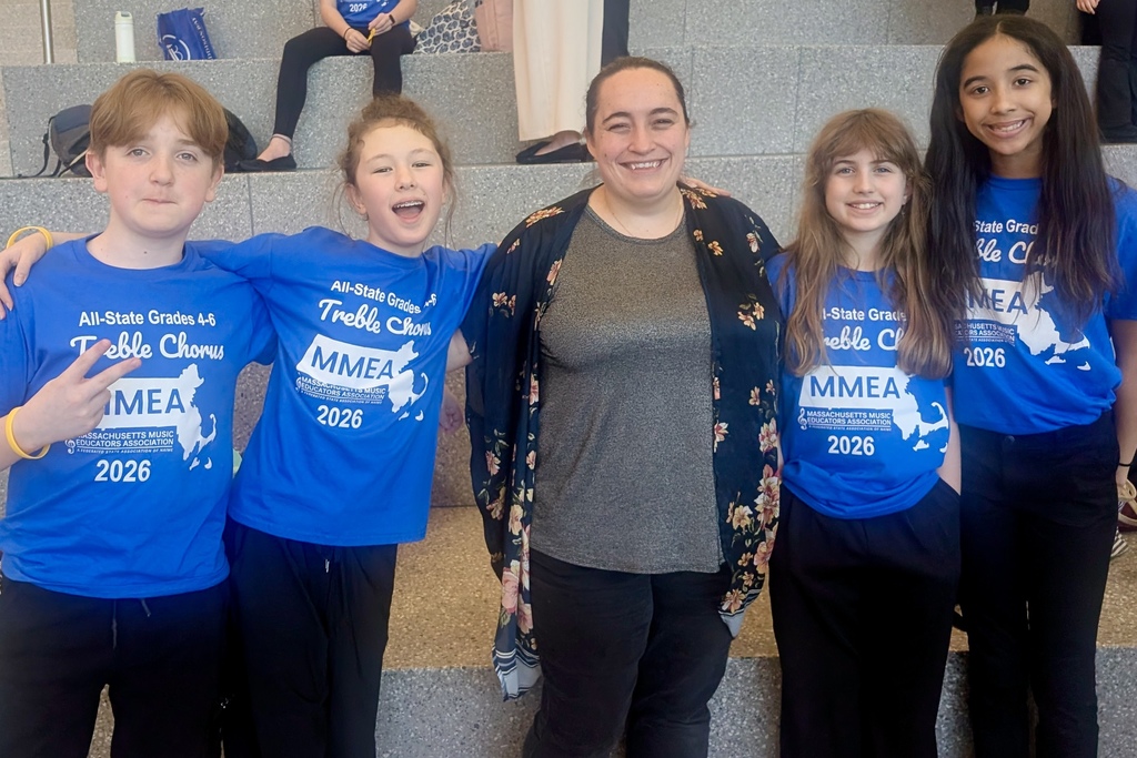 Five smiling children and an adult pose for a photo, all wearing blue shirts with "All-State Grades 4-6 Treble Chorus MMEA 2026" printed on them.