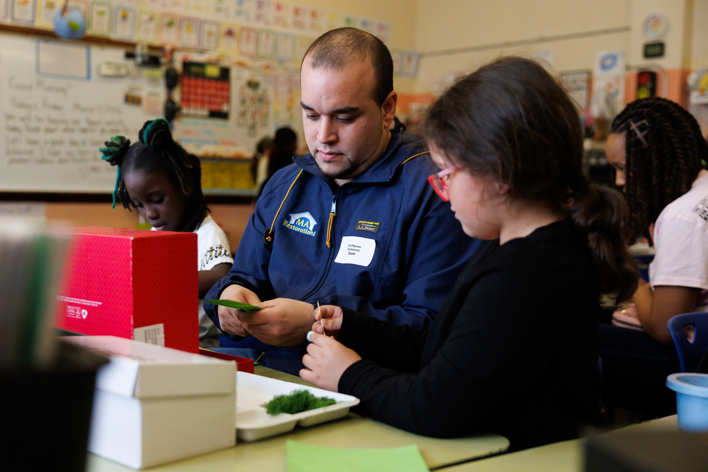 A parent helps their child cut construction paper for their 3D habitat,