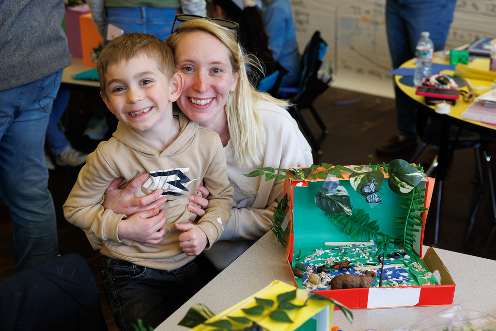 A parent and student smile behind their 3D habitat during a school activity.