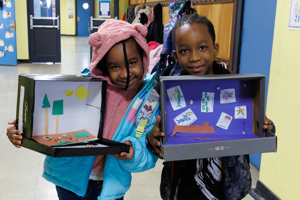 Two siblings hold up their 3D habitats.