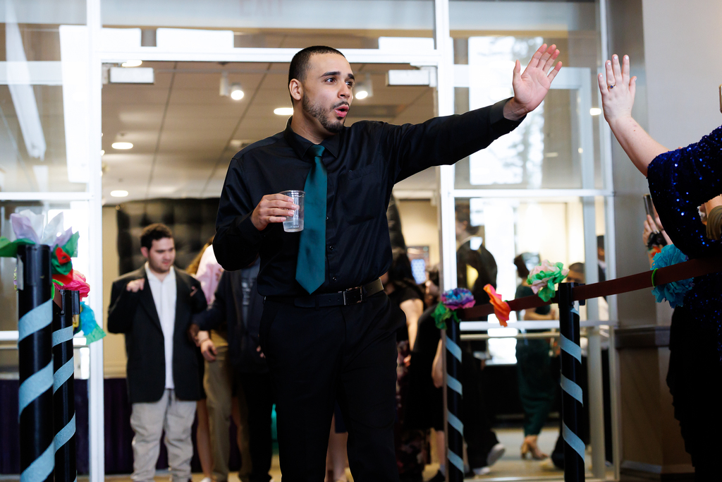 A student dressed in a black button up shirt and teal tie gives a high five to someone out of frame.