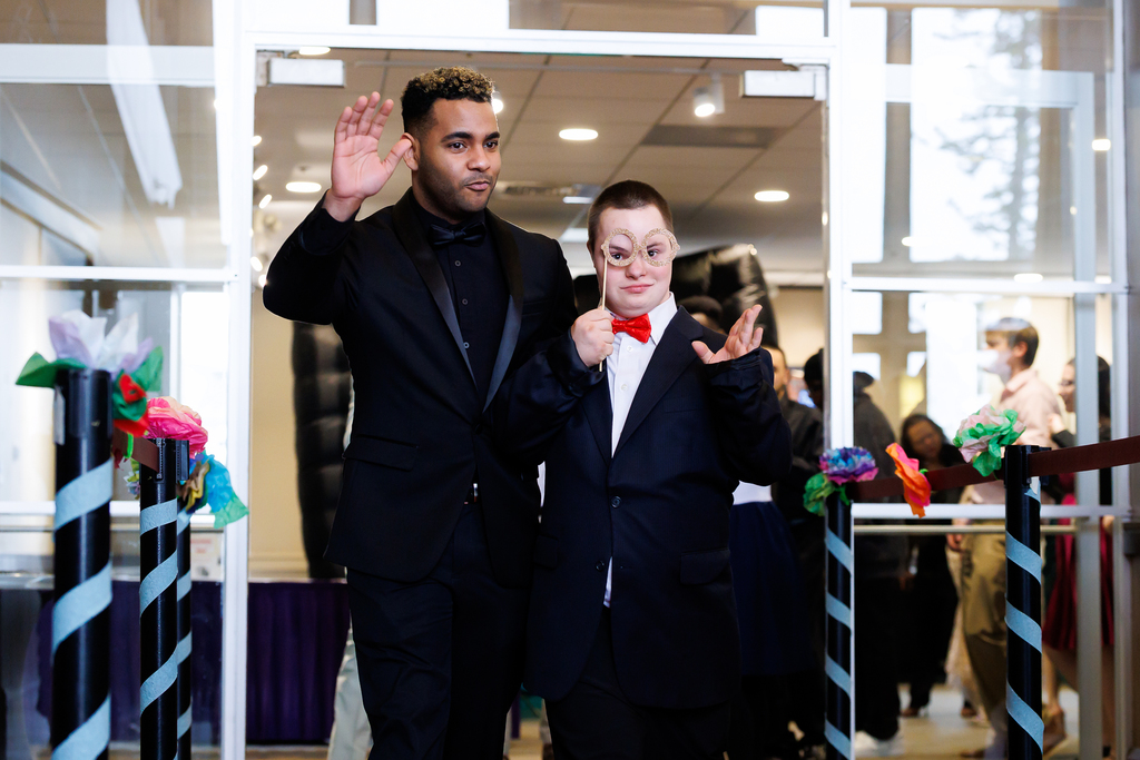 A student and a paraeducator walk together down the red carpet.