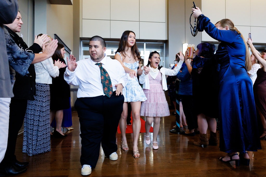 Two students walk down a red carpet alongside a student during a formal event.