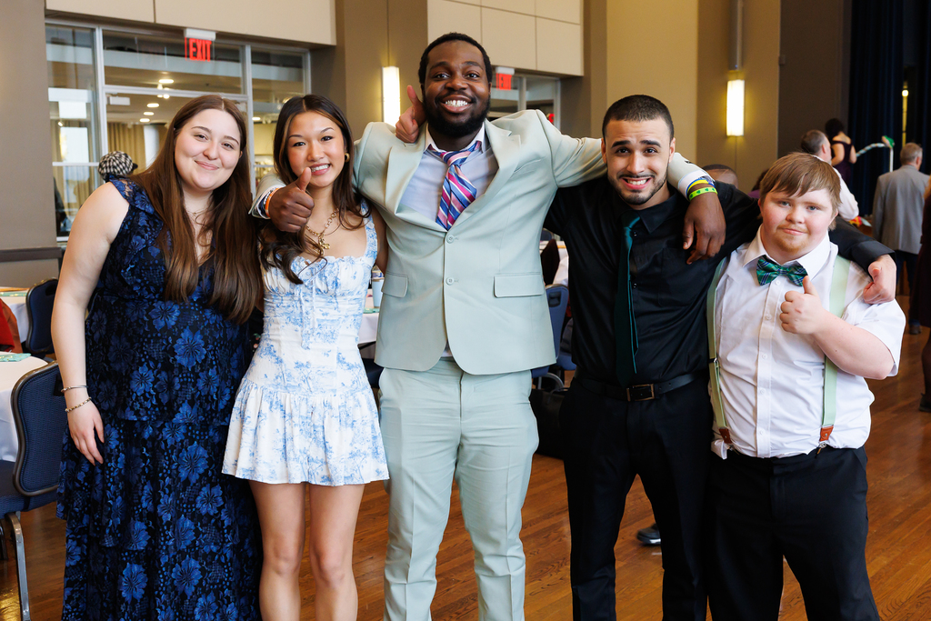 Five people stand together and smile for a photo.