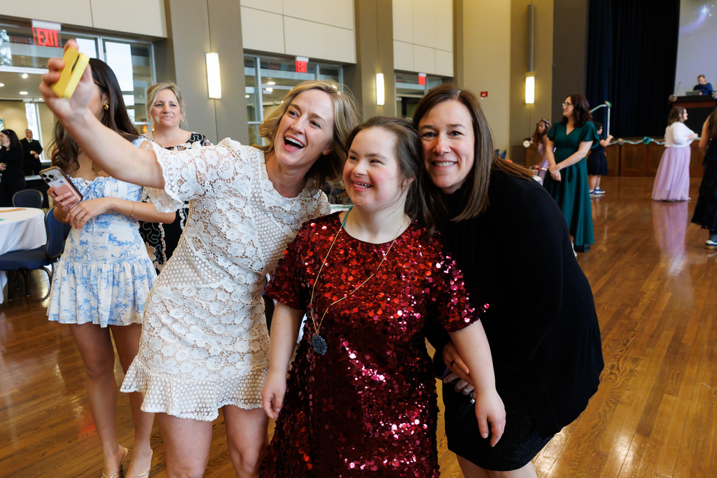 Two teachers take a selfie with a student during a formal event.