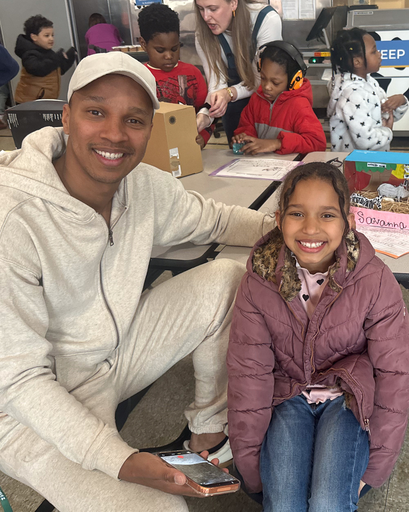 A father and daughter sit side by side and smile for a photo.