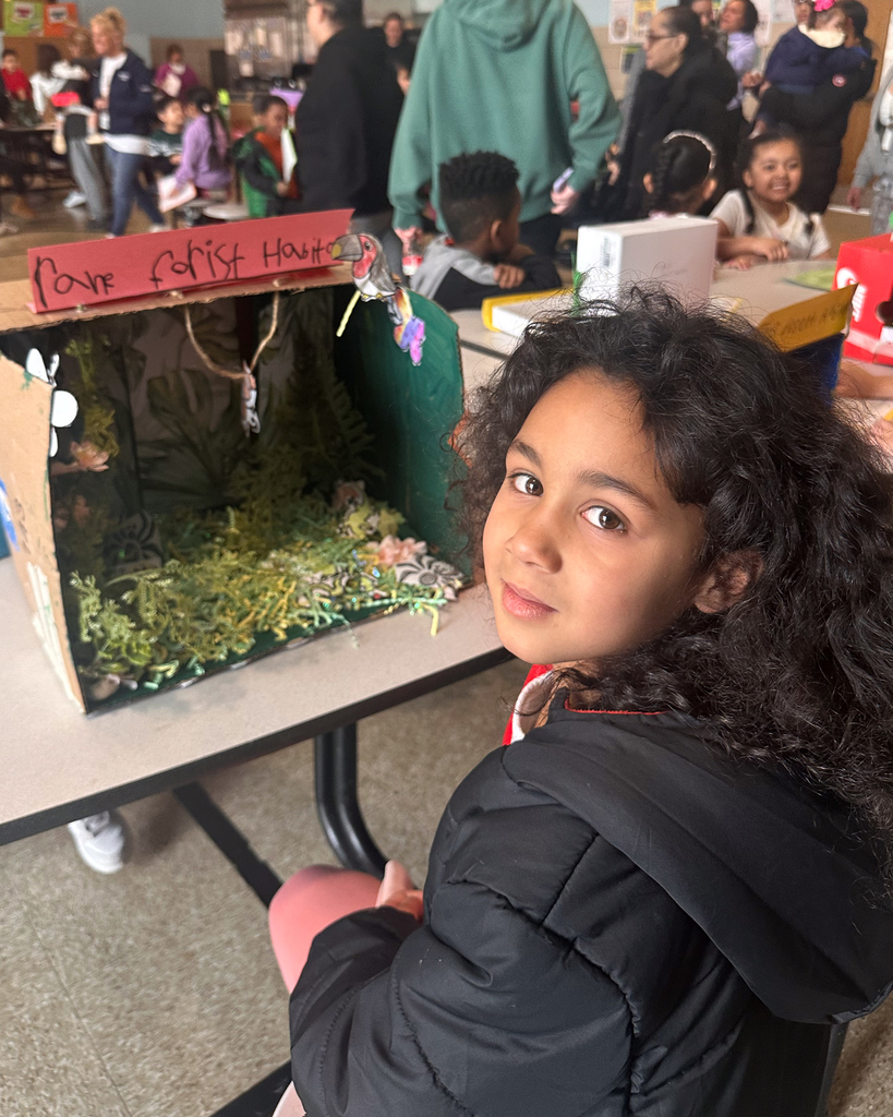 One student looks at the camera for a photo while sitting near their 3D Habitat.