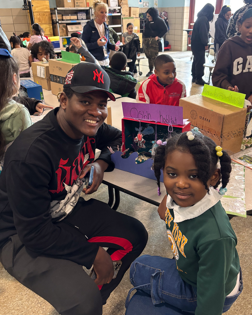 A father and daughter sit side by side and smile for a photo behind their 3D habitat.