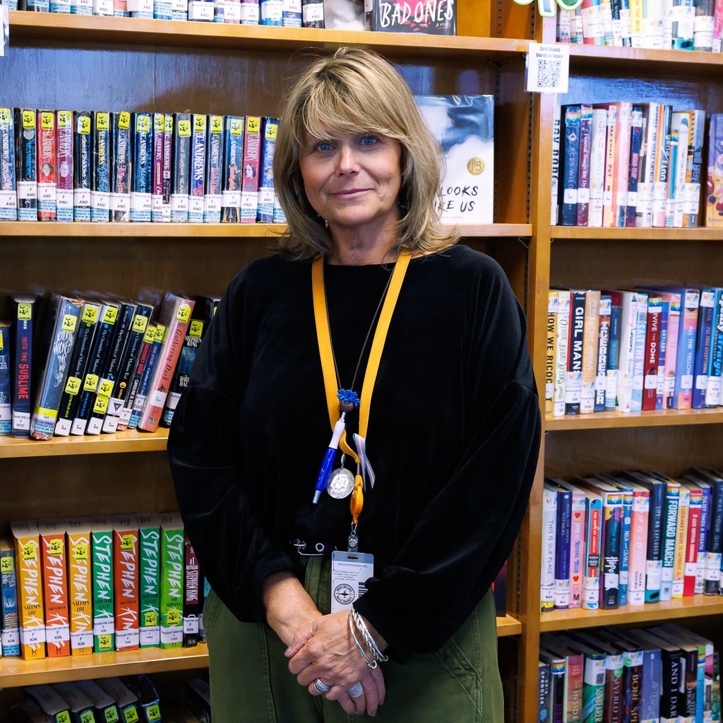 A woman with blonde hair stands in front of bookshelves filled with books.