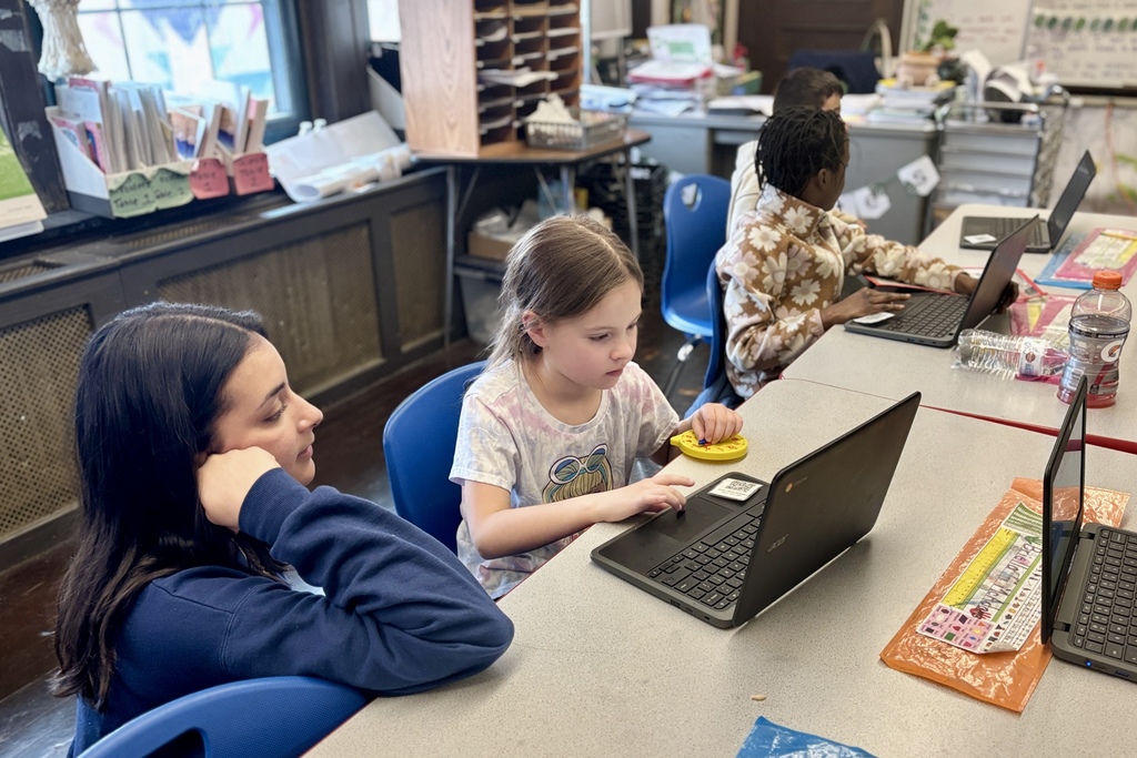 Students work on laptops at desks in a classroom setting.