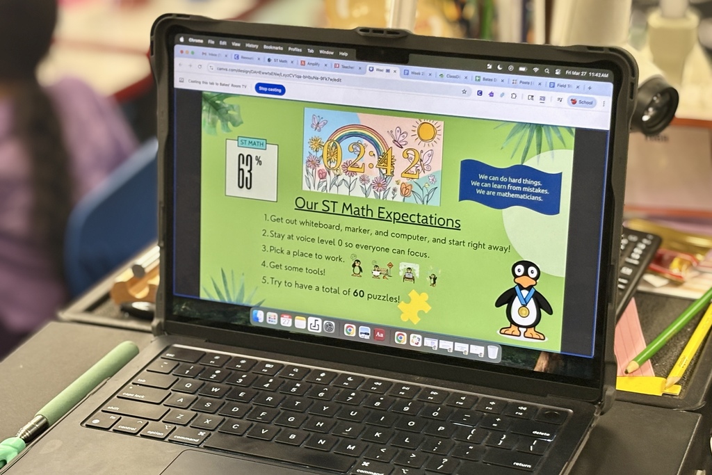 A laptop displays a colorful ST Math presentation with a penguin mascot and learning expectations.