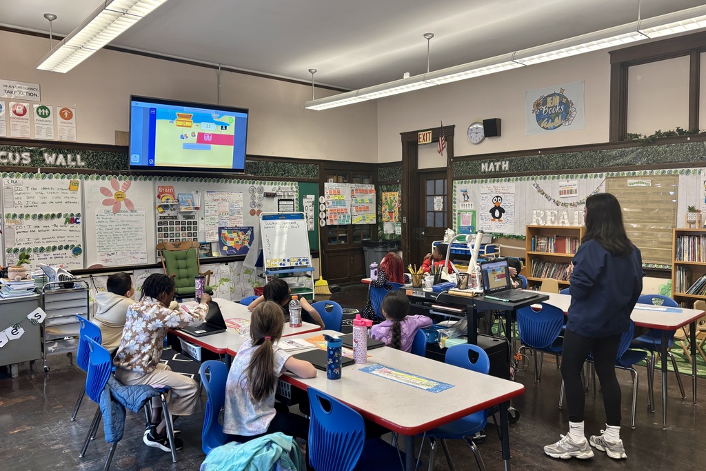 Students are engaged in a lesson in a brightly decorated classroom with a large screen displaying educational content.