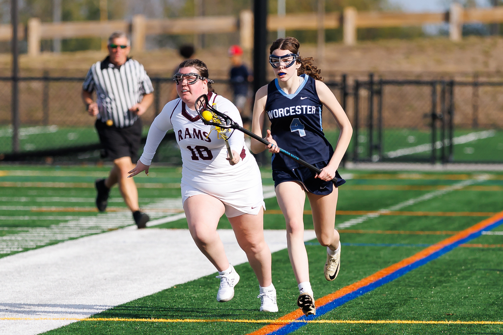 A player runs down the sidelines with the ball on her stick with a defender trailing close by.