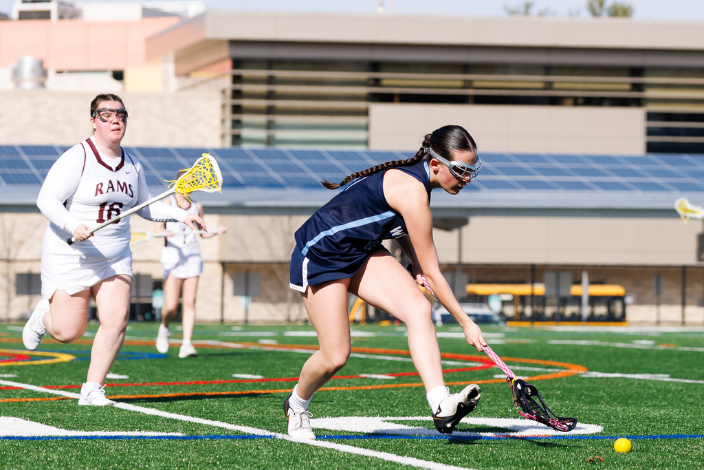 A lacrosse player scoops a loose ball up off the turf.