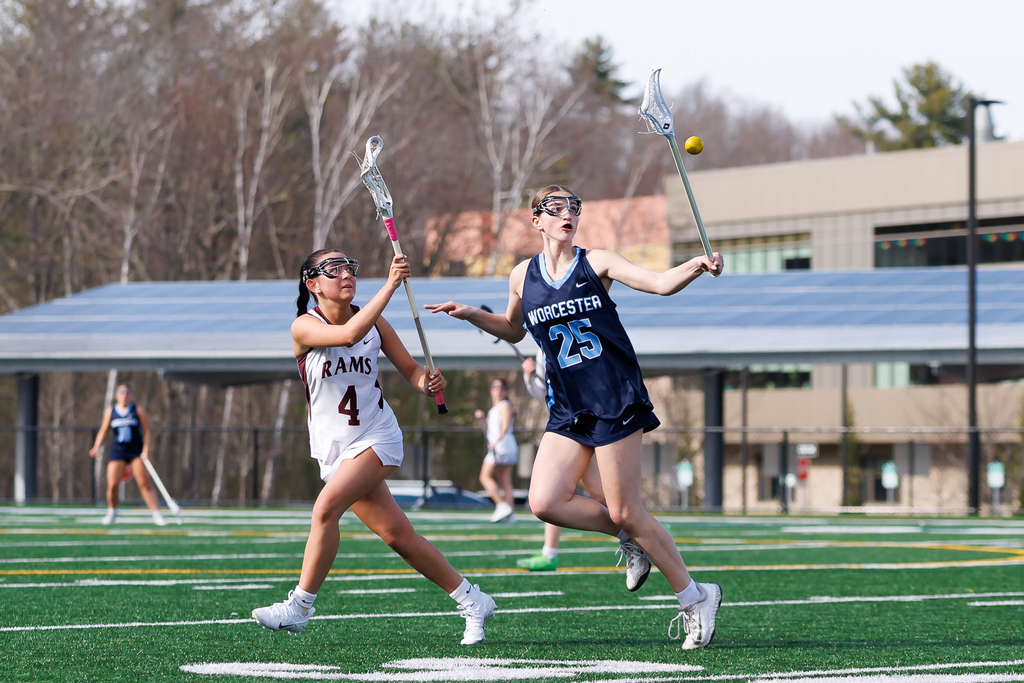 A lacrosse player raises her stick to deflect a pass with an opposing player close by.