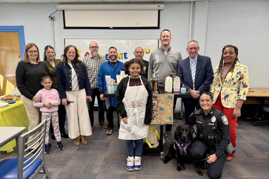 A group of adults and children pose for a photo with a service dog in front of a banner that reads 'CELEBRATE'.