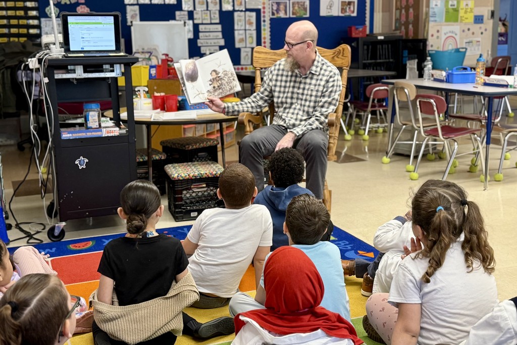A teacher reads a book to a group of young students sitting on the floor in a classroom.