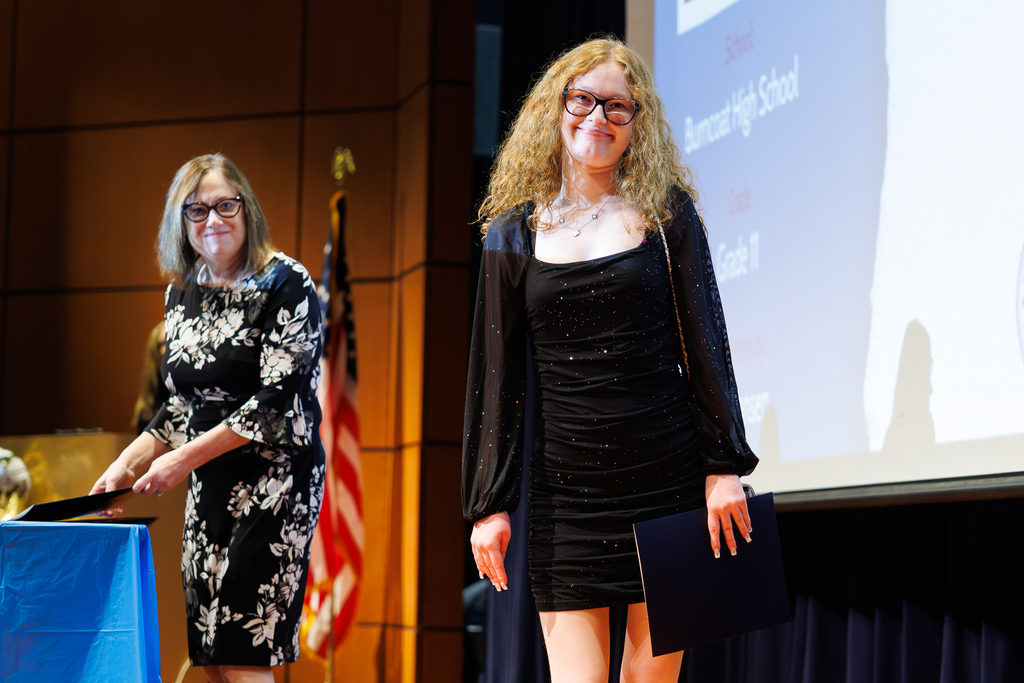 A student smiles while walking across the stage during a recognition event.