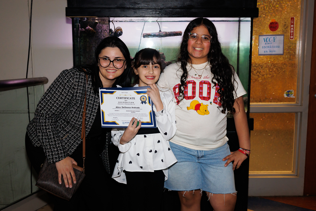 A family of three stand together and smile for a photo.