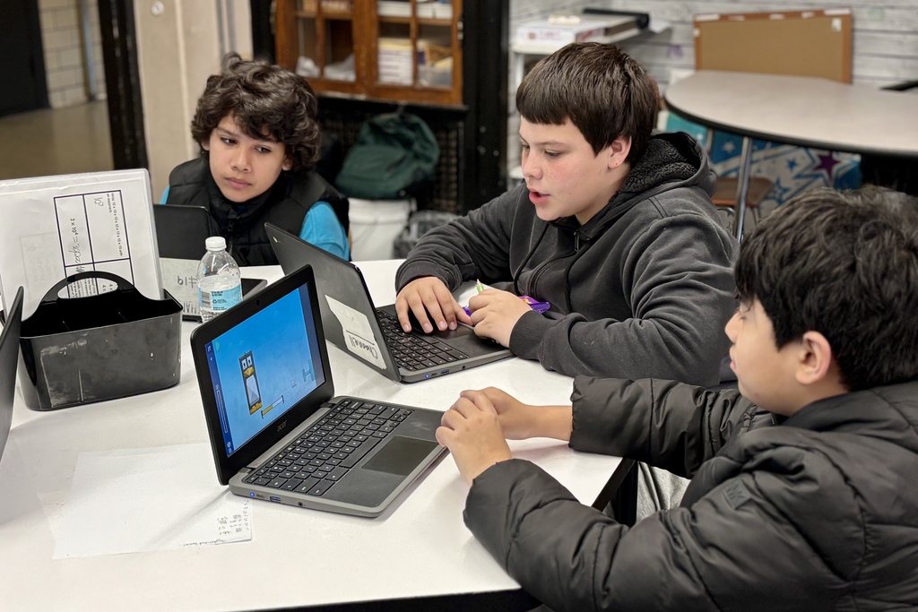 Three students focus on their laptops in a classroom setting, engaged in learning.