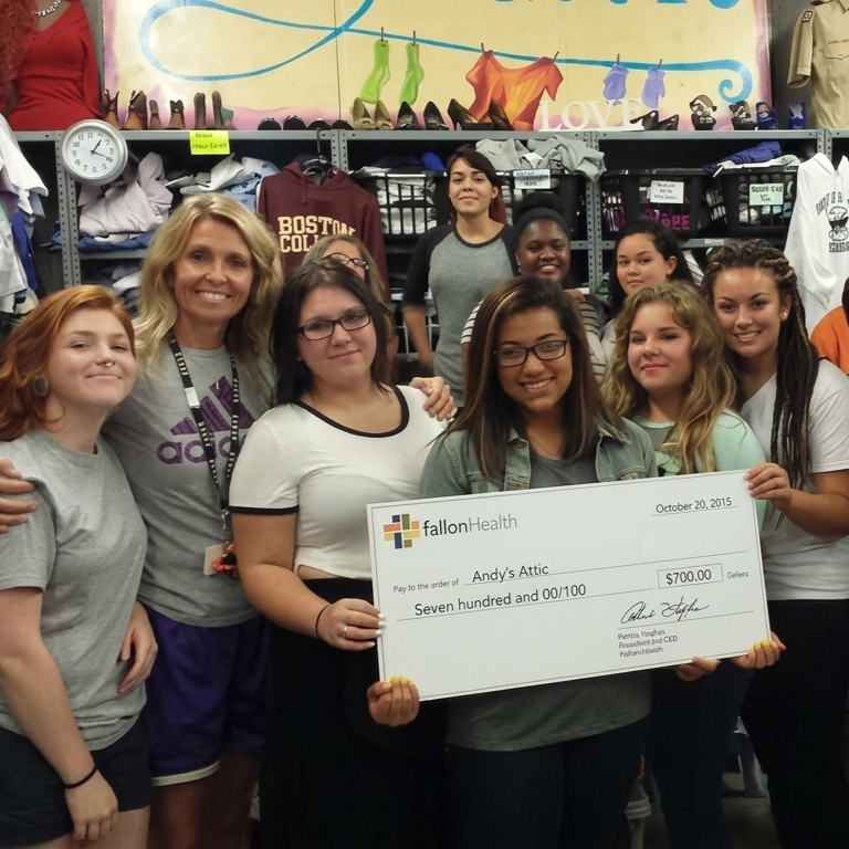 A group of women and girls pose for a photo, holding a large check for $700.00 made out to Andy's Attic.