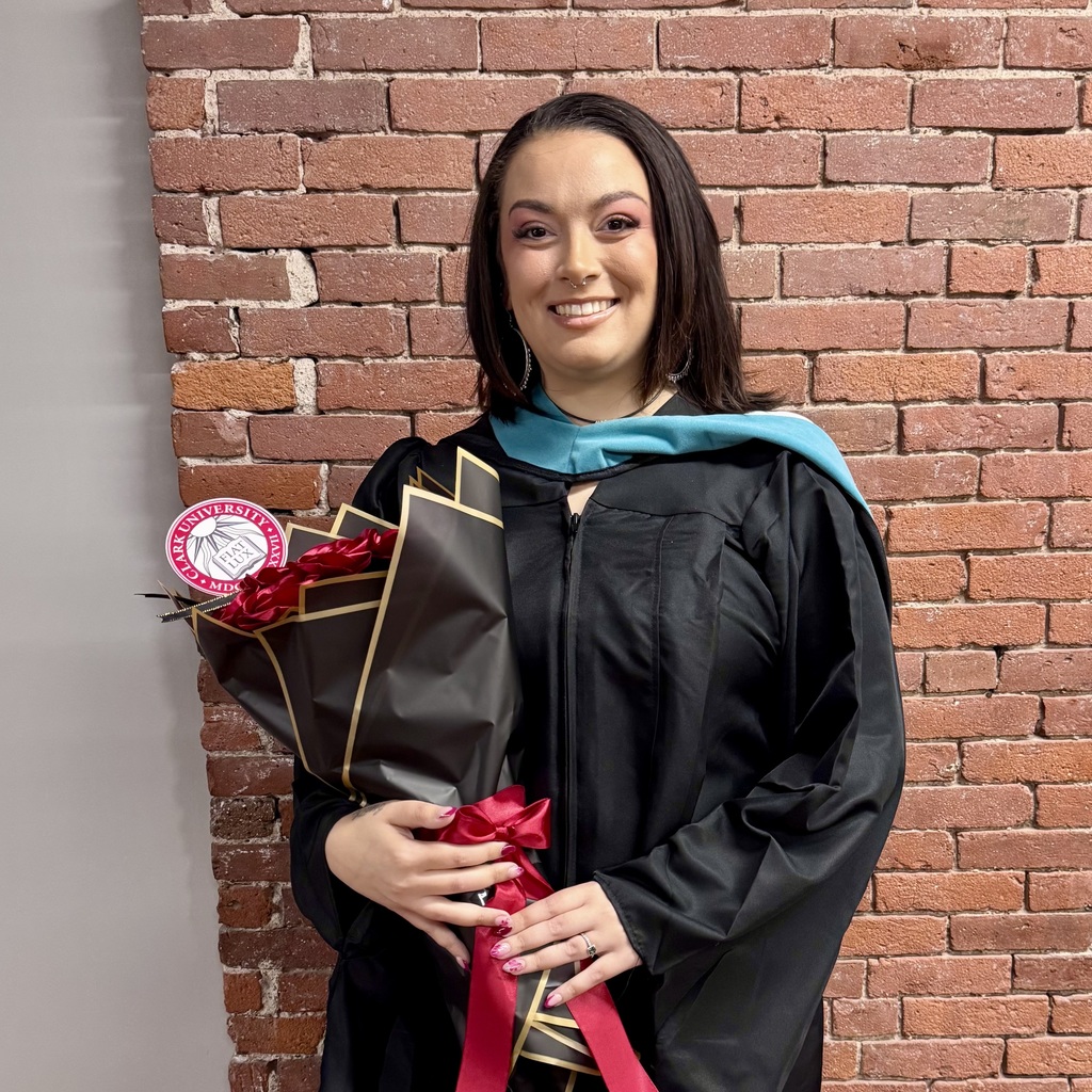 A smiling graduate in a black cap and gown holds a bouquet of red roses.
