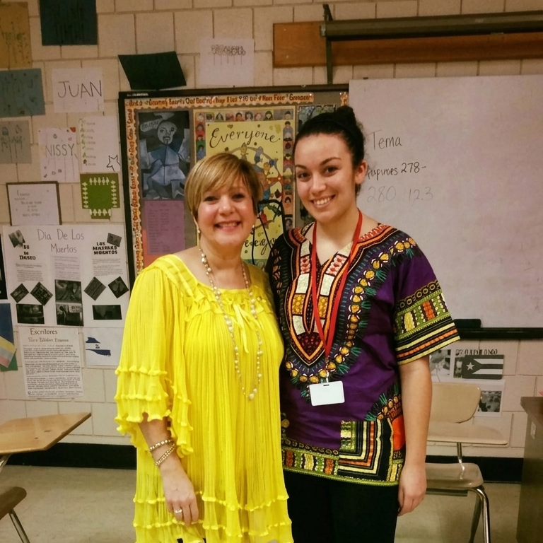 Two smiling women stand in a classroom with colorful decorations and a whiteboard.