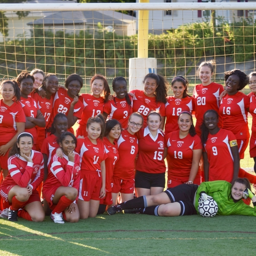 A diverse group of young women in red soccer uniforms pose for a team photo on a grassy field.