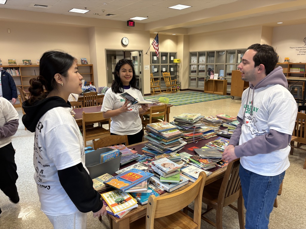 Three students standing in front of a table of books