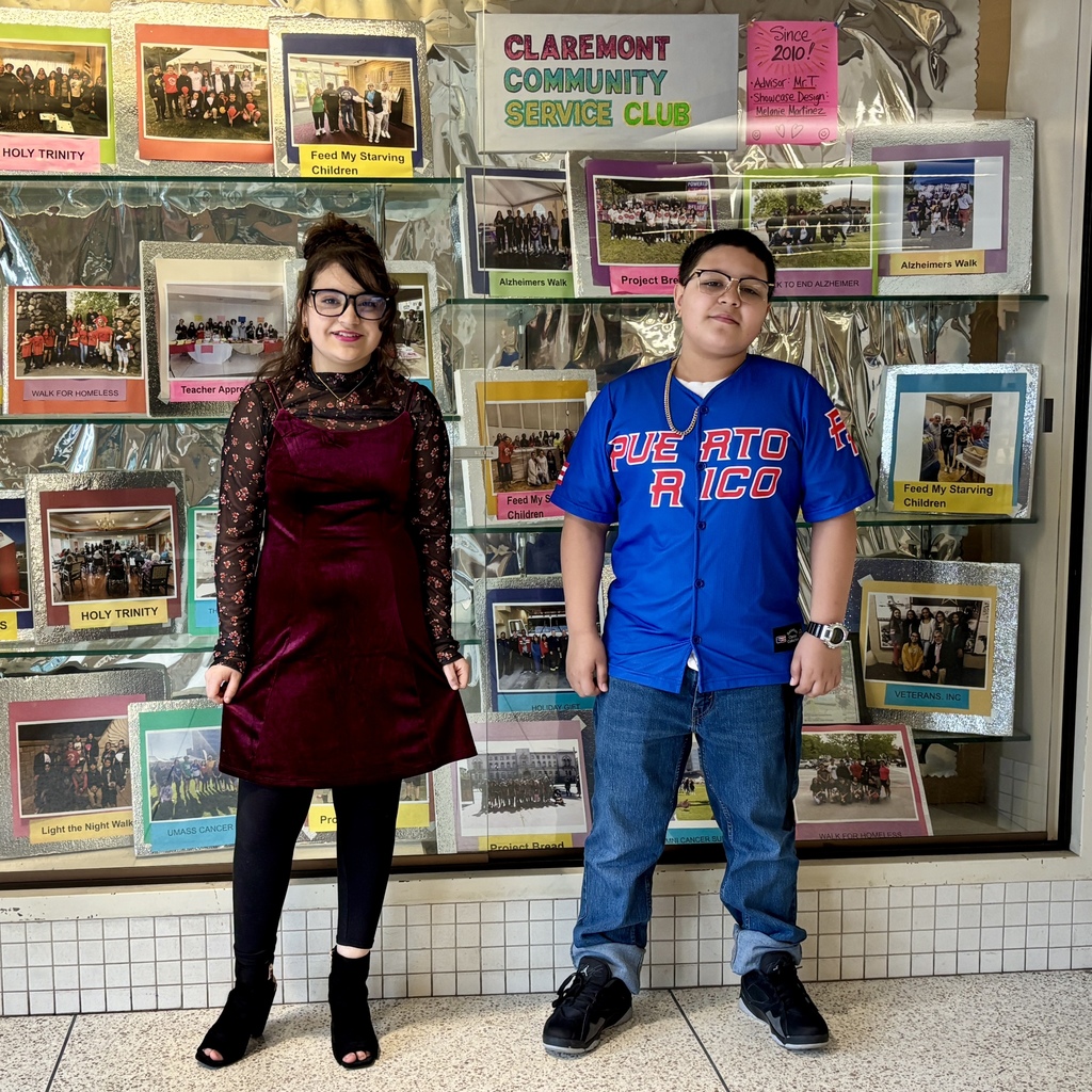 Two young people stand in front of a display showcasing photos and text from the Claremont Community Service Club.