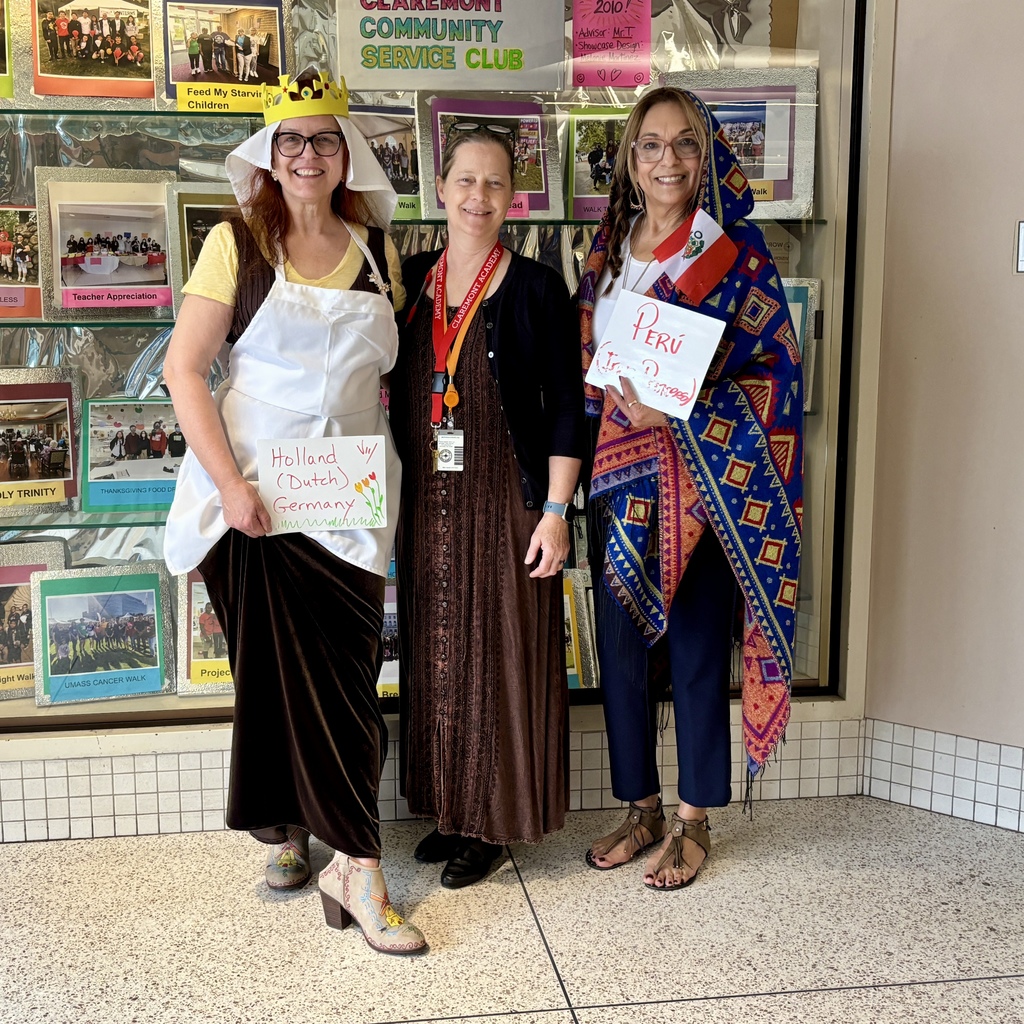 Three women stand in front of a display board, two holding signs representing Holland/Germany and Peru.