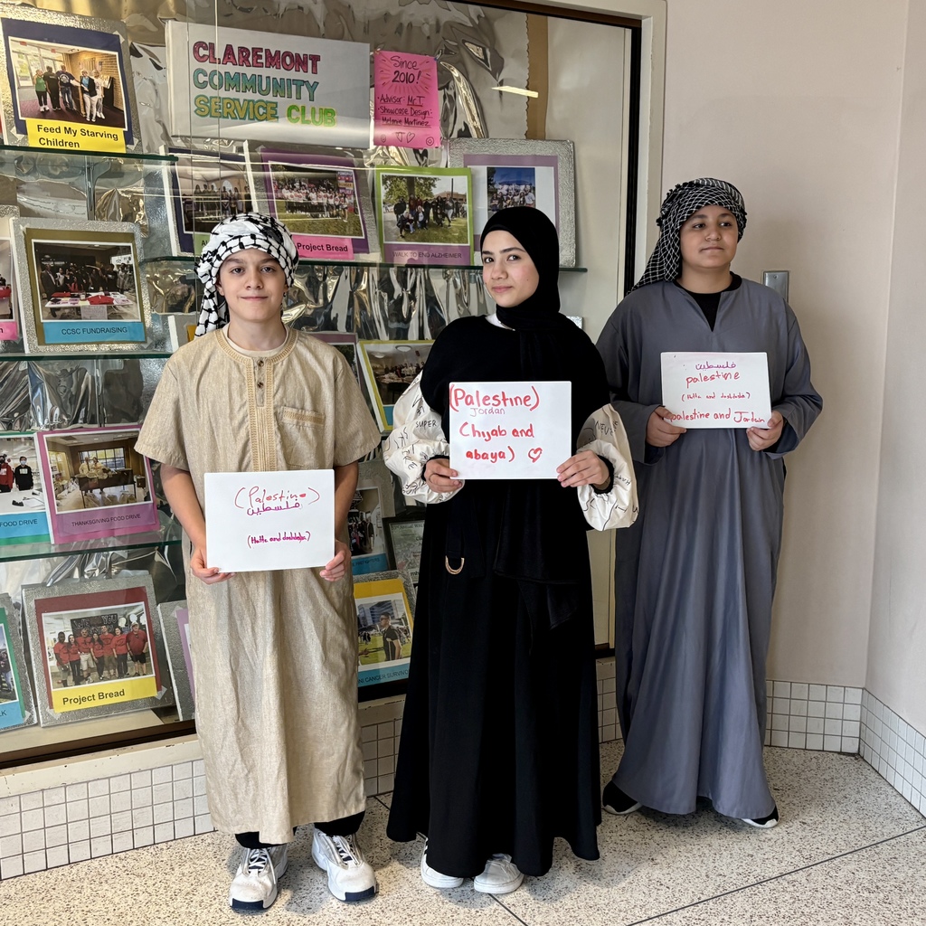 Three young people stand in front of a display board, holding signs about Palestine and Jordan.
